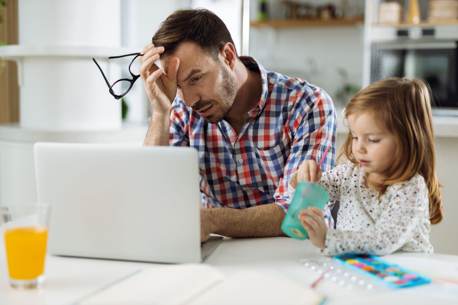 Father using laptop for telehealth while family life continues around him