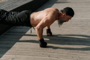 Senior man with a beard exercising outdoors, performing push-ups on a wooden deck.