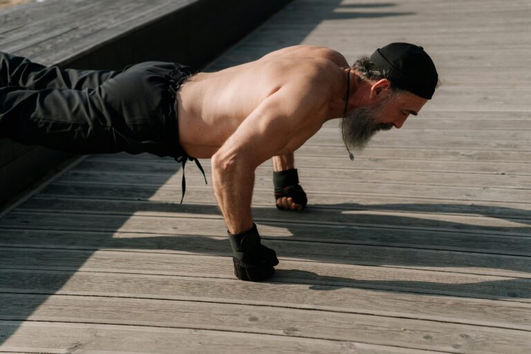 Senior man with a beard exercising outdoors, performing push-ups on a wooden deck.